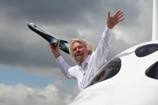 richard branson hanging out of an airplane holding a small replica spaceship