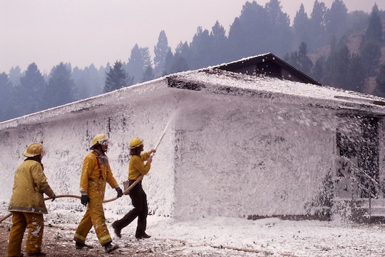 Three firefighters coat a small house in foam during a wildfire. 