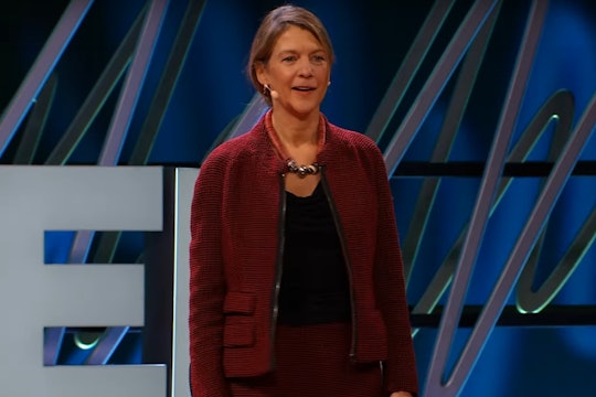 heidi larson, a woman wearing a red suit, standing on stage to give a talk