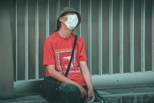 A man wearing a red shirt and a face mask leans back on a bench looking dejected