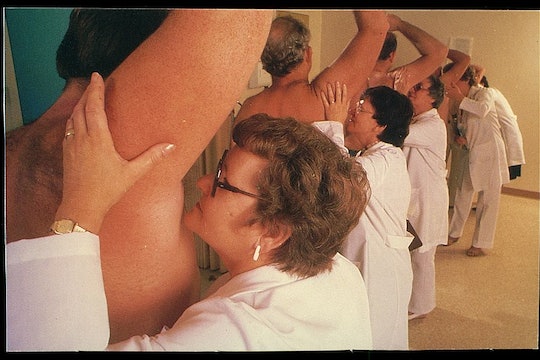 a line of women wearing lab coats smelling the armpits of a bunch of men