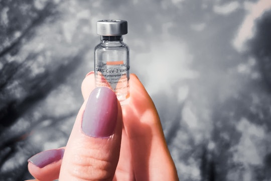 a woman's hand holding a vial of vaccine against a sky backdrop