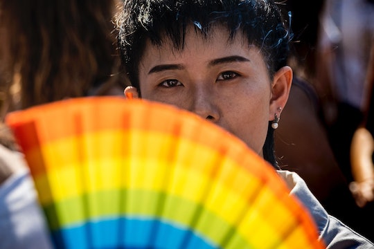 A person looks out from behind a rainbow-colored fan.